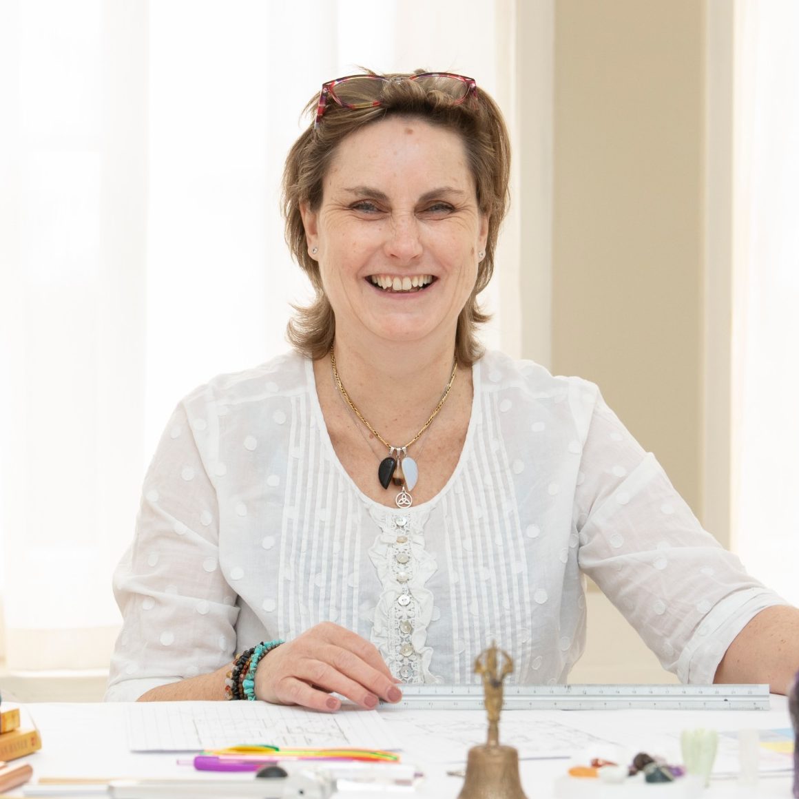 Smiling woman seated at a table surrounded by arts and crafts materials.