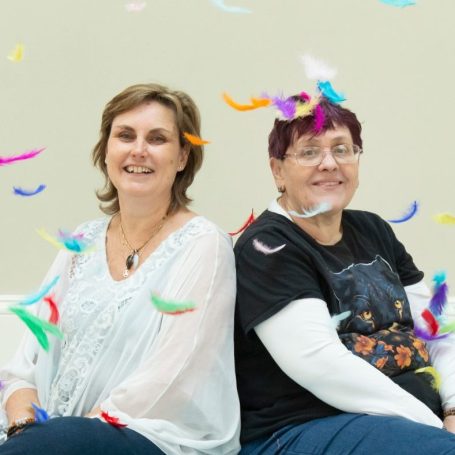 Two women sitting side by side, smiling, surrounded by colourful confetti.